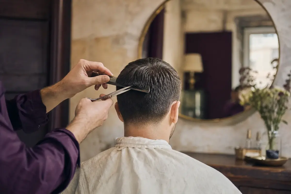 A stylist finishing a short men's cut, client seen from behind