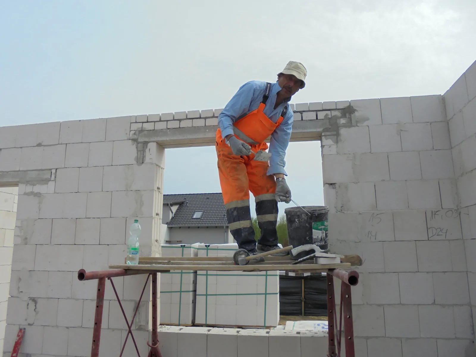 DX bricklayer in orange overalls on scaffolding beside a sand-lime block wall