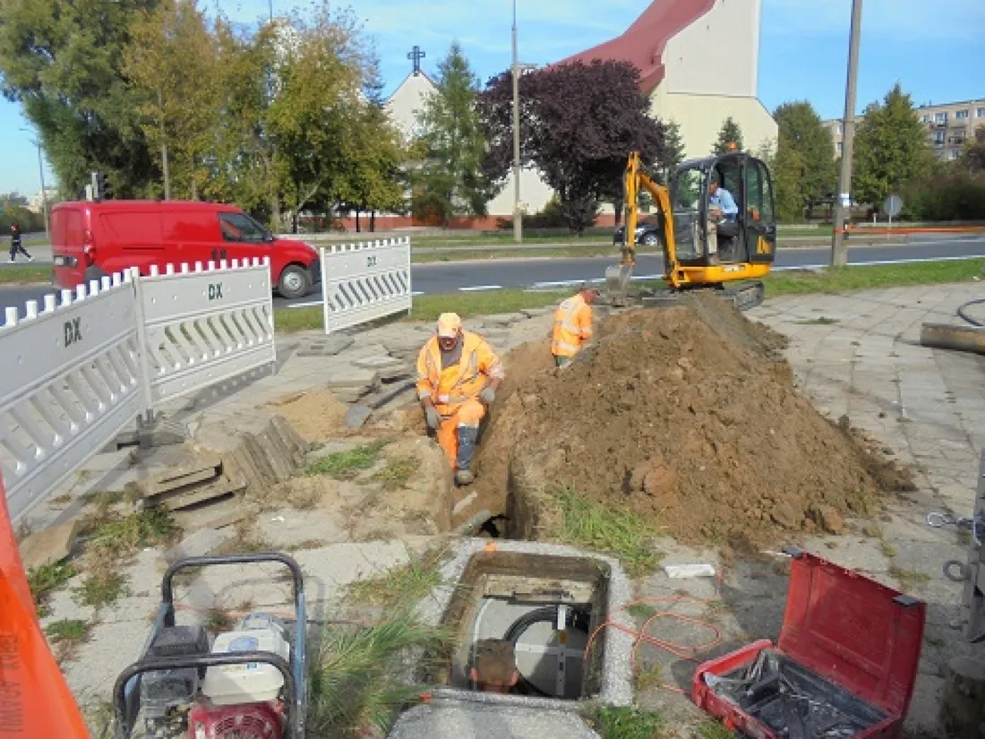 Trench for ducting along a street, mini digger in the background