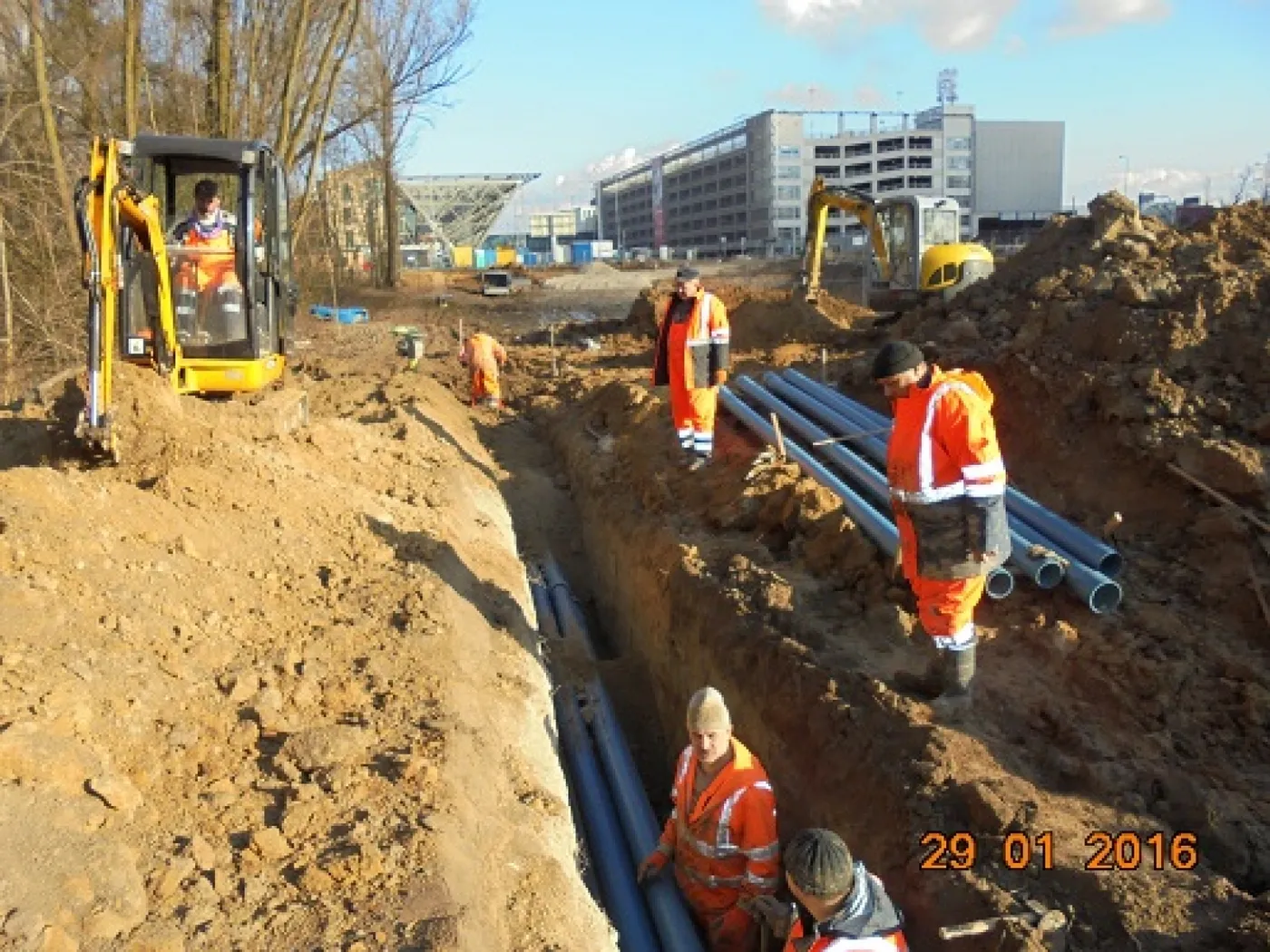 Trench with protective ducts for an MV network, mini digger and crew in the background