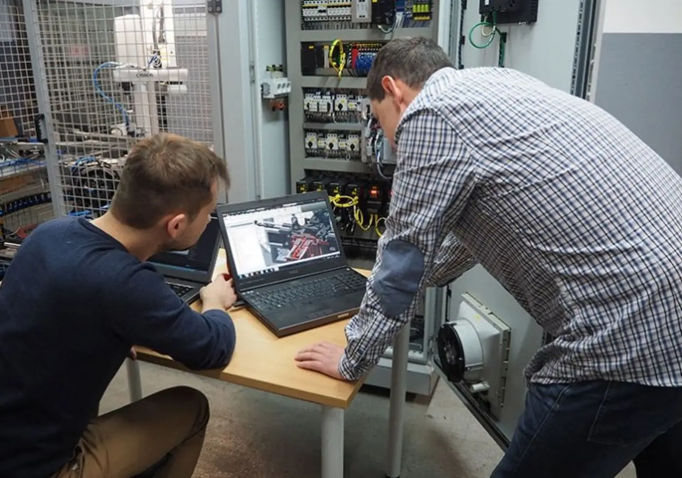 Welmasz engineers programming a machine at a control cabinet